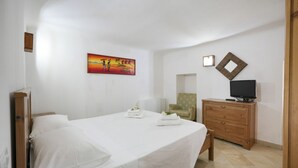 Ein Schlafzimmer mit Bett, Sessel, Kommode, Fernseher und einem Bild an der Wand.