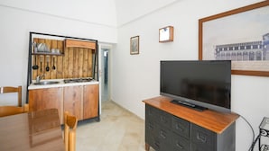 Ein kompakter Wohnbereich mit Küchenzeile, Essbereich und einem Flachbildfernseher auf einem Holzschrank.