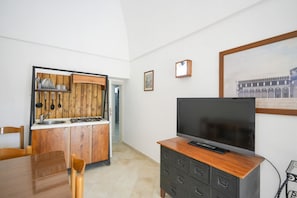 A compact living space with a kitchenette, a dining area, and a flat-screen TV on a wooden cabinet.
