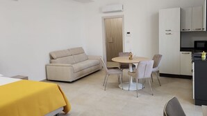 Une pièce moderne et bien éclairée, comprenant un canapé, une table à manger, des chaises et un coin cuisine.