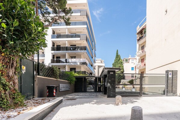 A multi-story building with balconies, a gated entrance, and a clear sky.