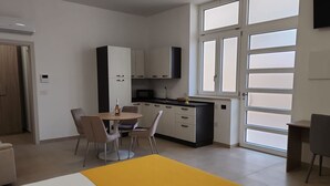 Une cuisine moderne avec des meubles blancs, un coin repas agrémenté d’un tapis jaune et une grande fenêtre laissant entrer la lumière naturelle.