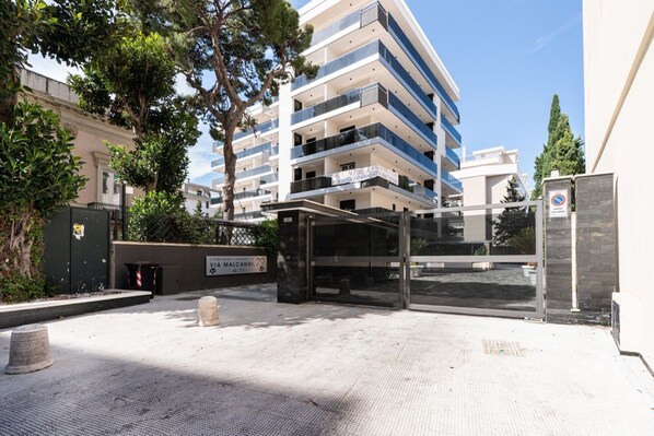 Un edificio de varios pisos con balcones, una entrada cubierta y un cartel que indica una ubicación.