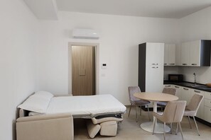 Una habitación compacta con cama, una pequeña mesa de comedor, sillas, kitchenette y una puerta.