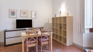 A room with a TV, a wooden table with chairs, and a bookshelf. - GuestHost - Cozy and quiet apartment of 60 sqm, for 4 people, located on the 1st floor of a building (no elevator). The property is located near Piazza Dalmazia, from where the tram leaves to reach in a few minutes the Santa Maria Novella Station and the (Florence)