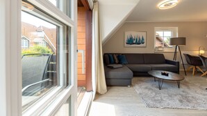 A modern living room with a sectional sofa, a round coffee table, and a floor lamp. There is a window with a view of a brick building outside.