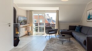 A modern living room with a fireplace, a sofa, a coffee table, and a view of a residential area through large windows.
