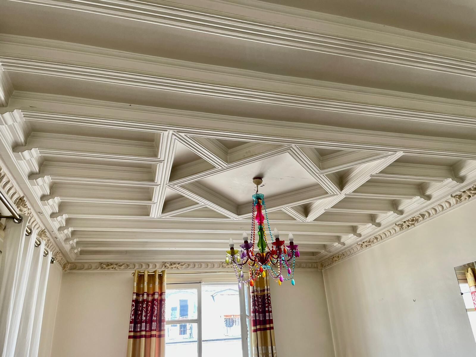A room with a high ceiling featuring decorative moldings and a chandelier.