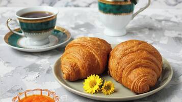 A marble table with a plate of croissants, a cup of coffee, and a vase of yellow flowers.