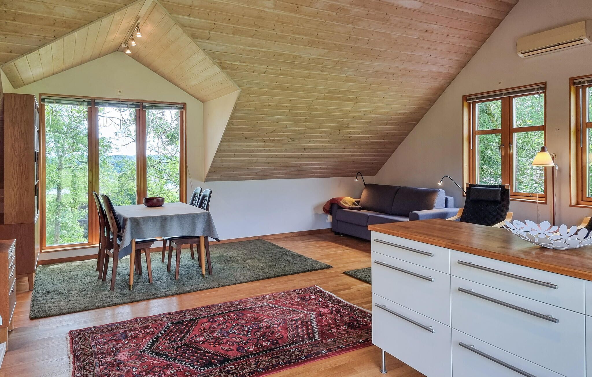 Una habitación con techo inclinado, una mesa de comedor con sillas, un sofá y un mueble con cajones.