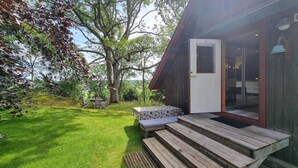 A wooden deck with a table and chairs, a covered outdoor seating area, and a view of the surrounding greenery and trees. - 1 bedroom awesome home in Västerlanda (Västerlanda)