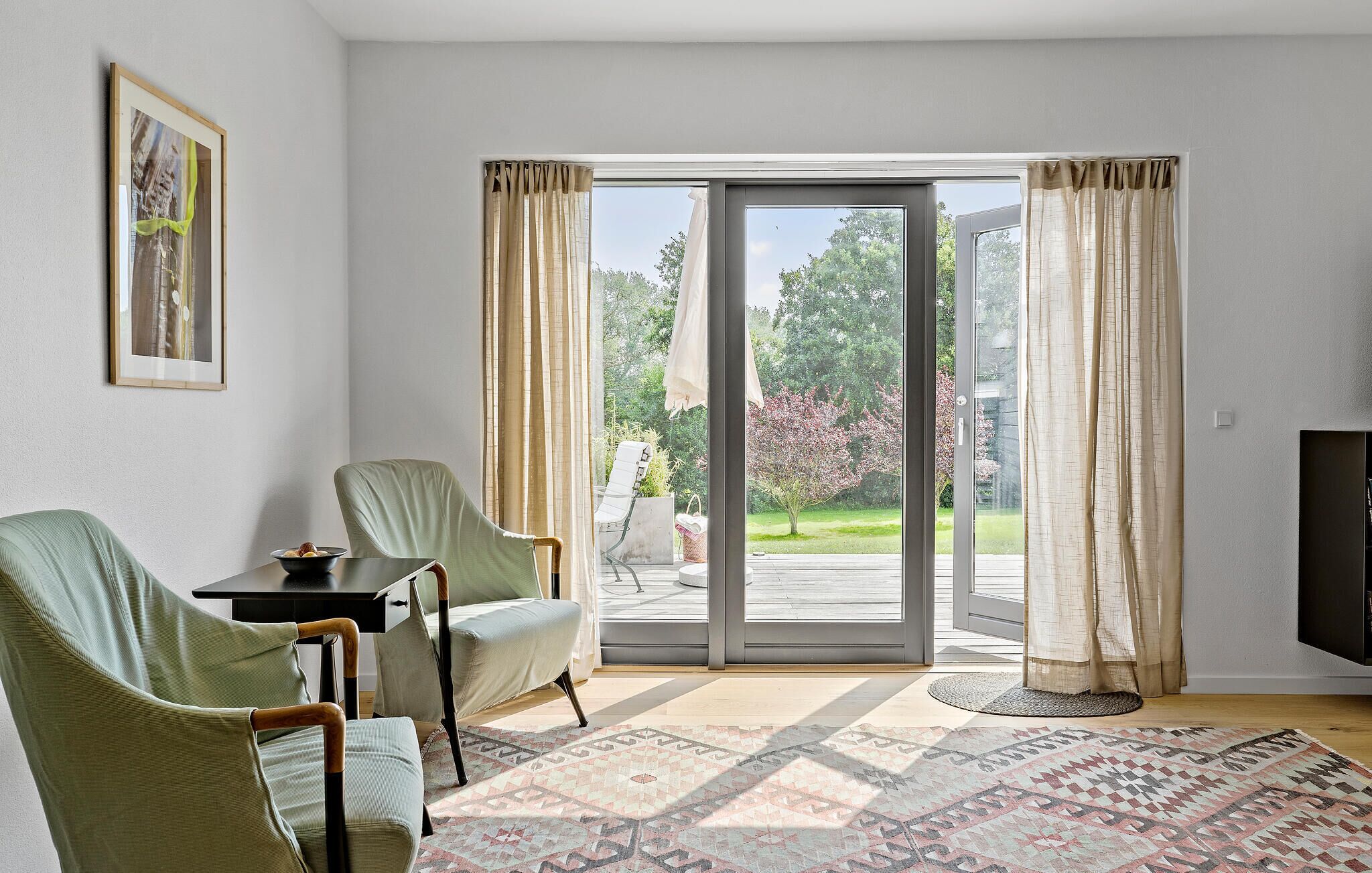 A living room with a large sliding glass door leading to a garden, two chairs, a small table, and a TV.