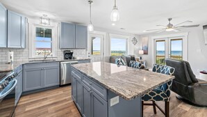 A modern kitchen with a large island, grey cabinets, and a view of the ocean.