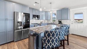 A modern kitchen with grey cabinets, stainless steel appliances, a marble island, and bar stools.