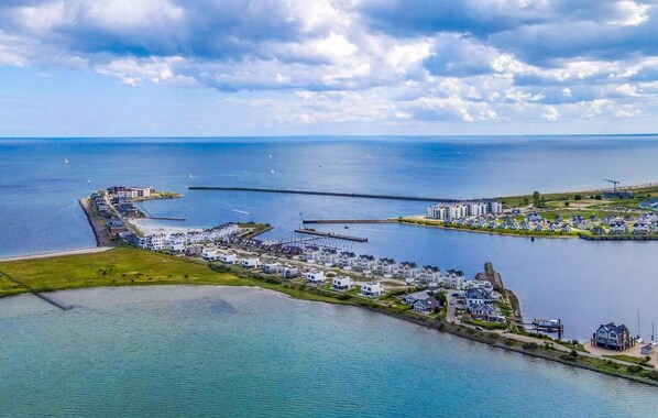 Vista aérea de un pueblo costero con un puerto deportivo, edificios residenciales y un muelle que se adentra en el agua.