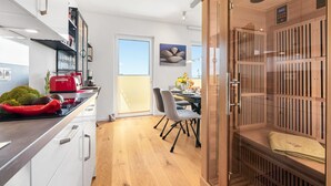 Une cuisine moderne avec des meubles blancs, une bouilloire rouge et un coin repas comprenant une table et des chaises.