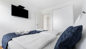 Une chambre moderne avec un lit, des murs blancs, un téléviseur fixé au mur et une porte donnant sur une autre pièce.