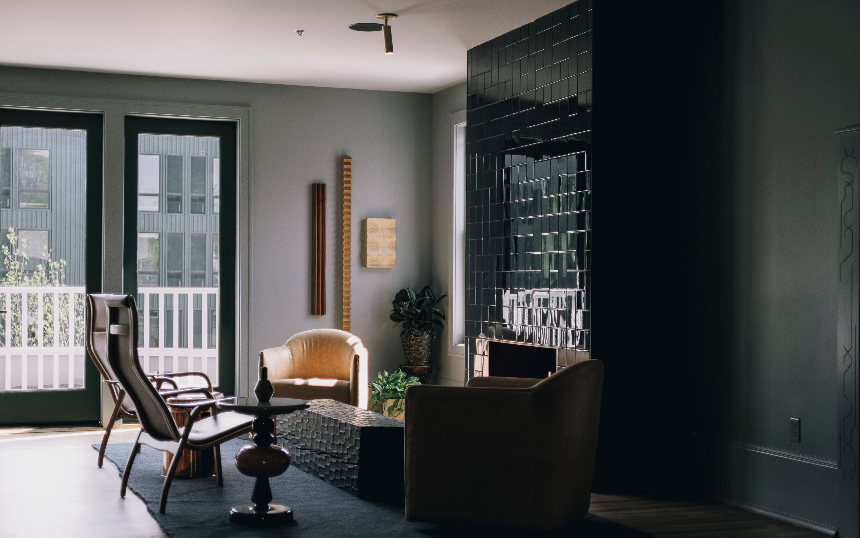 A modern living room with a sofa, chairs, a coffee table, and a large window with black tiles.