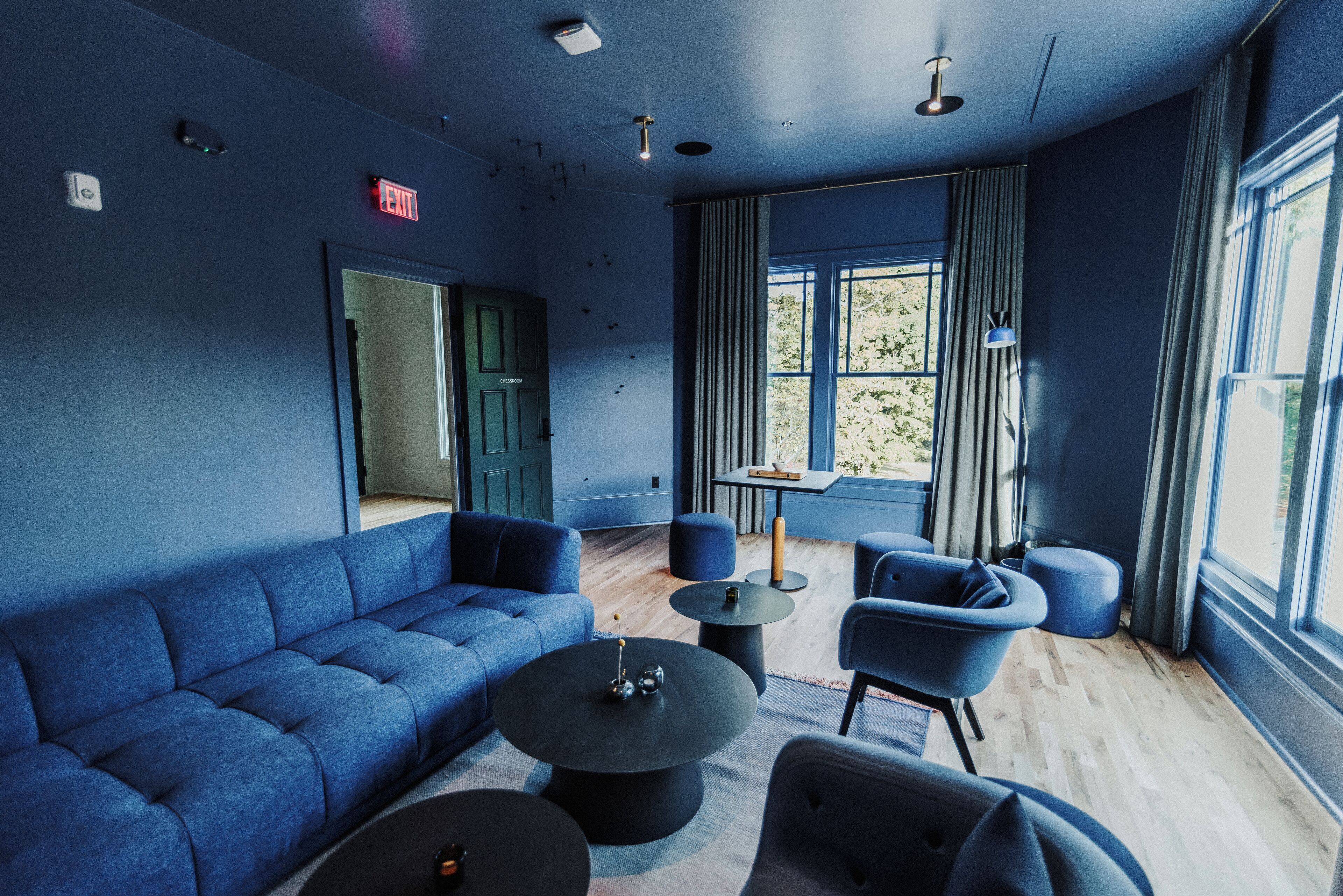 A modern lounge area with a blue sofa, round tables, and a large window with curtains.