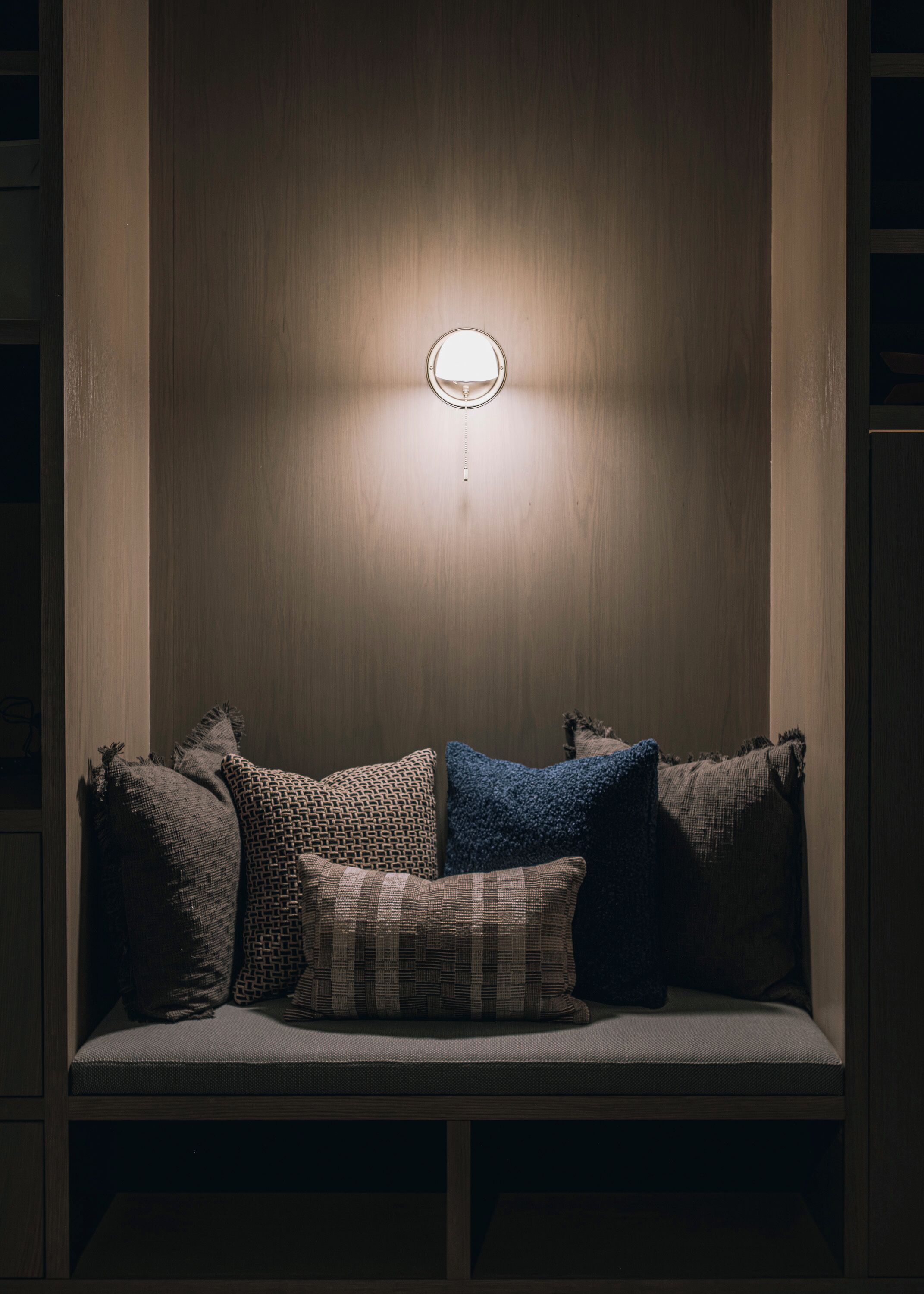 A dimly lit room with a wooden wall and a bench with cushions.