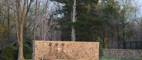 A stone-built outdoor fireplace with a stone wall and a paved pathway.