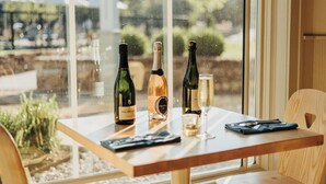 A table with three wine bottles and a glass, set against a window with a view of greenery and a building. - Stonebreaker Hotel (Fayetteville)