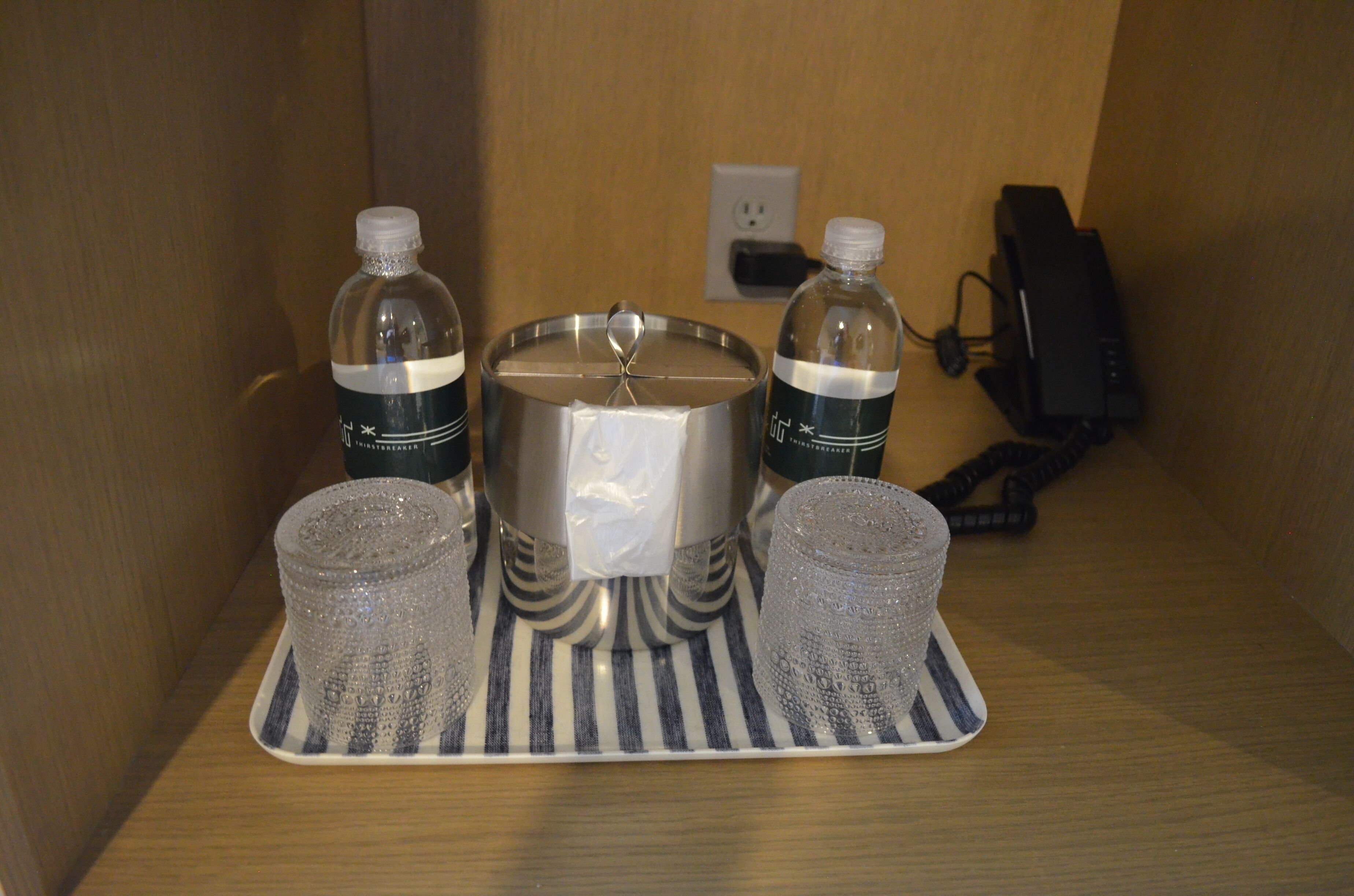 A small table with a metal container, two bottles, and two glasses.
