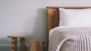 A bedroom with a wooden bed, a small wooden nightstand, a round wooden stool, and a wall-mounted light fixture.