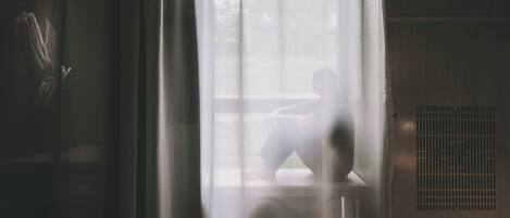 A room with a large window covered by sheer curtains, a radiator, and a wooden floor.
