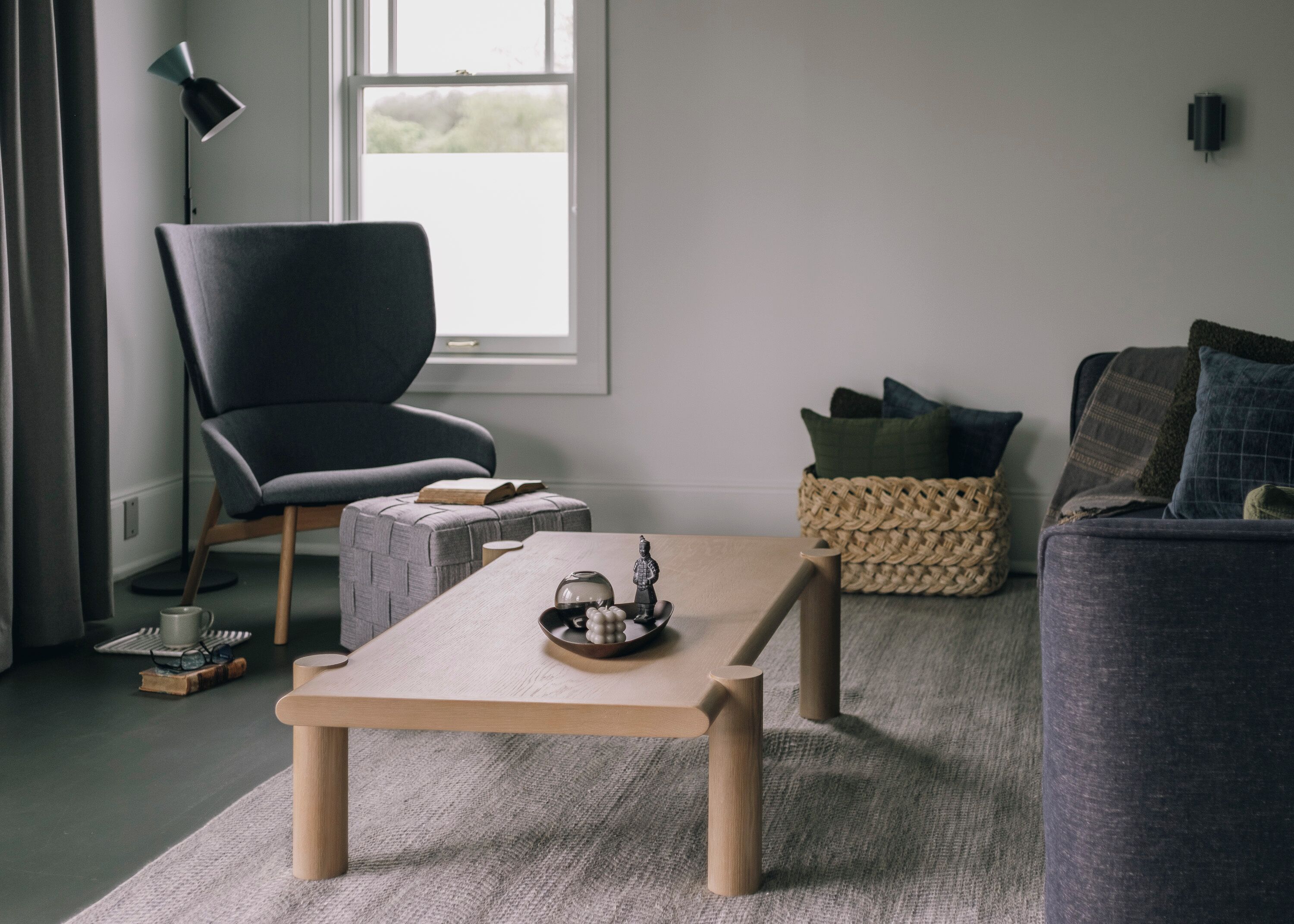 Un salon moderne avec un fauteuil gris, une table basse en bois, un lampadaire et un canapé agrémenté de coussins.