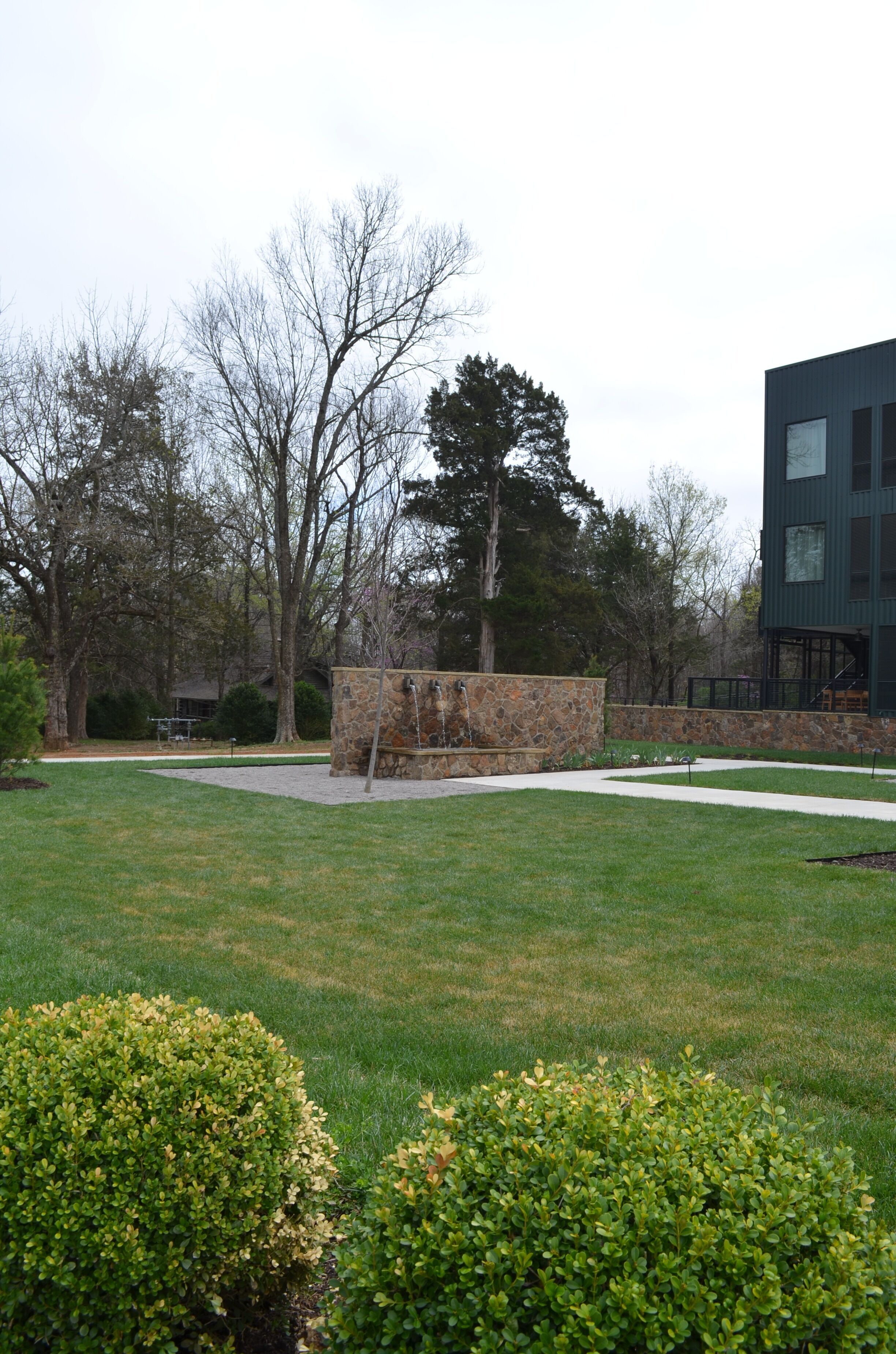 Une cour verdoyante avec une structure en pierre, des arbres et un bâtiment moderne.