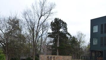 A grassy courtyard with a stone structure, trees, and a modern building.
