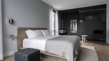 A modern bedroom with a large bed, a bedside table, a small stool, a chair, and a mirror.