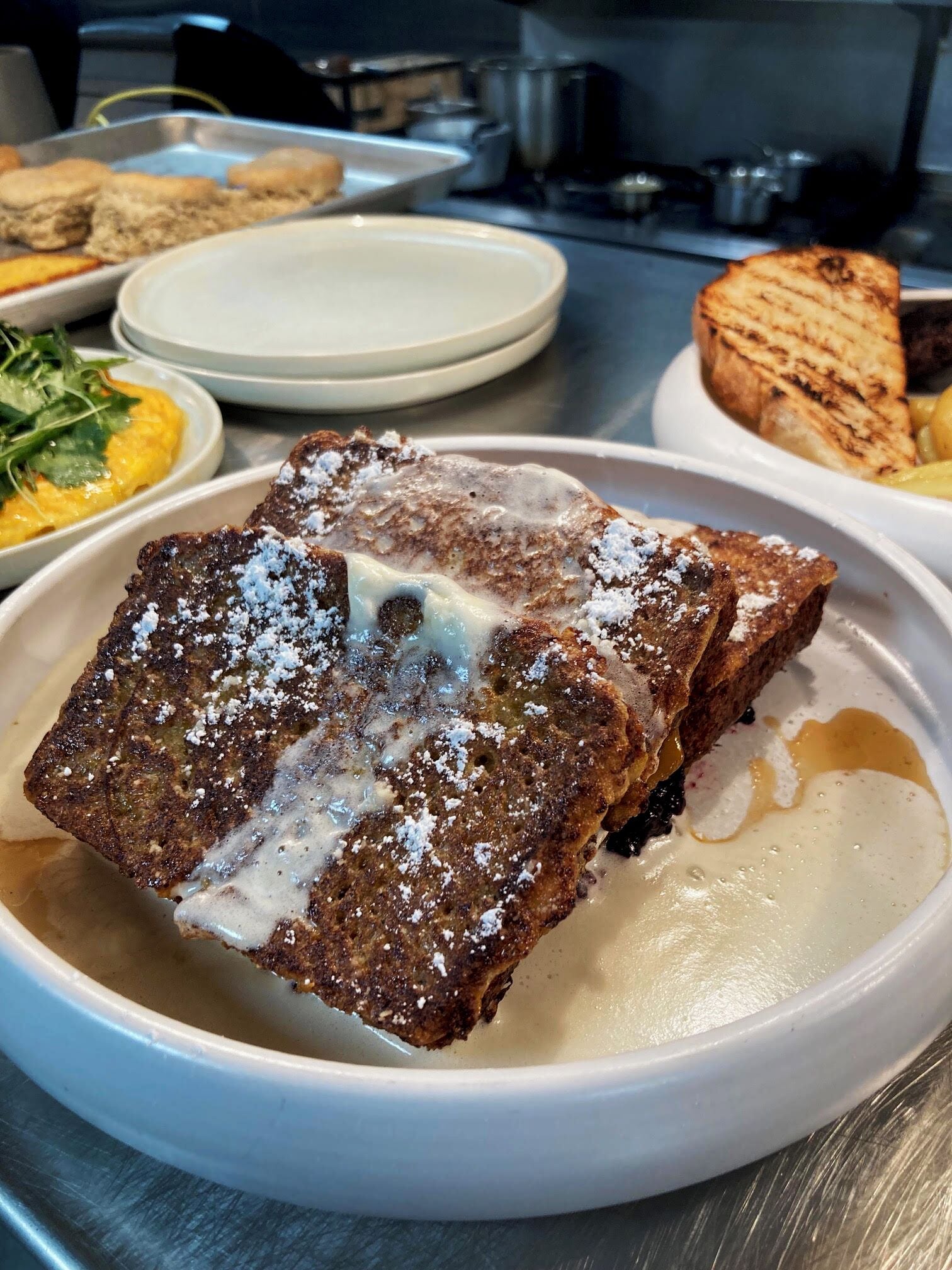 A breakfast plate with a piece of toast topped with butter and powdered sugar, accompanied by a side of scrambled eggs and greens.