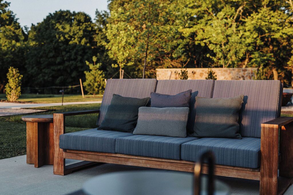 A wooden outdoor sofa with cushions, set on a concrete patio with a backdrop of trees.