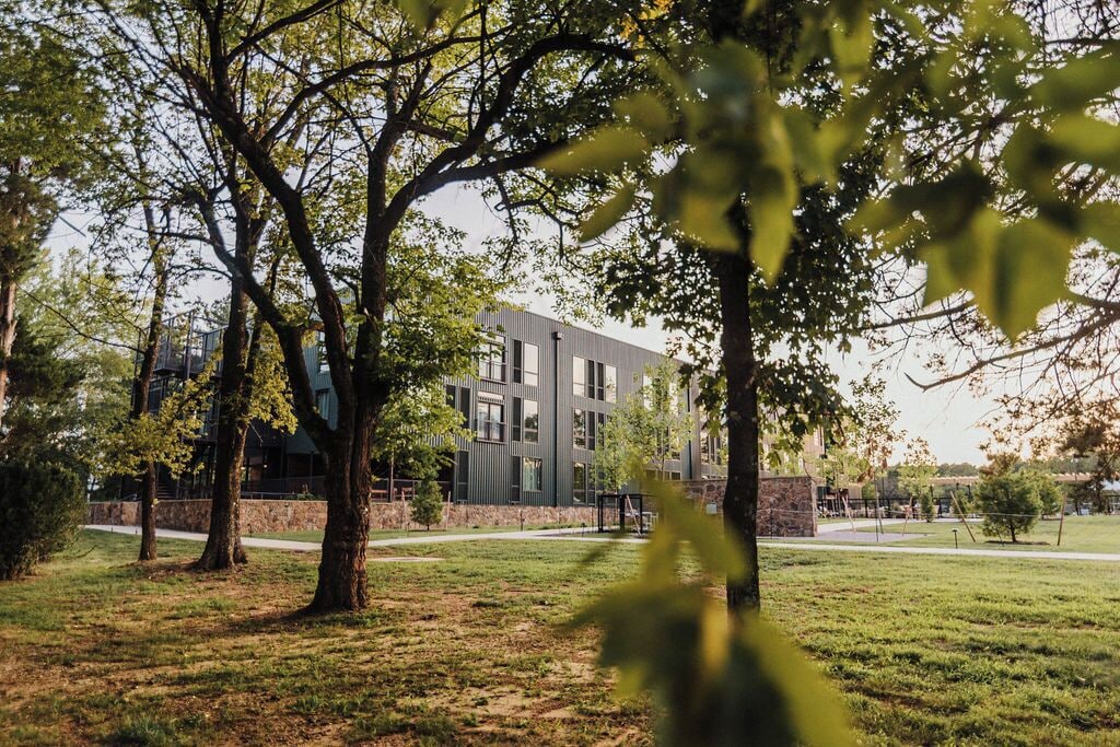 Un edificio moderno con fachada de vidrio, rodeado de un área verde con árboles.