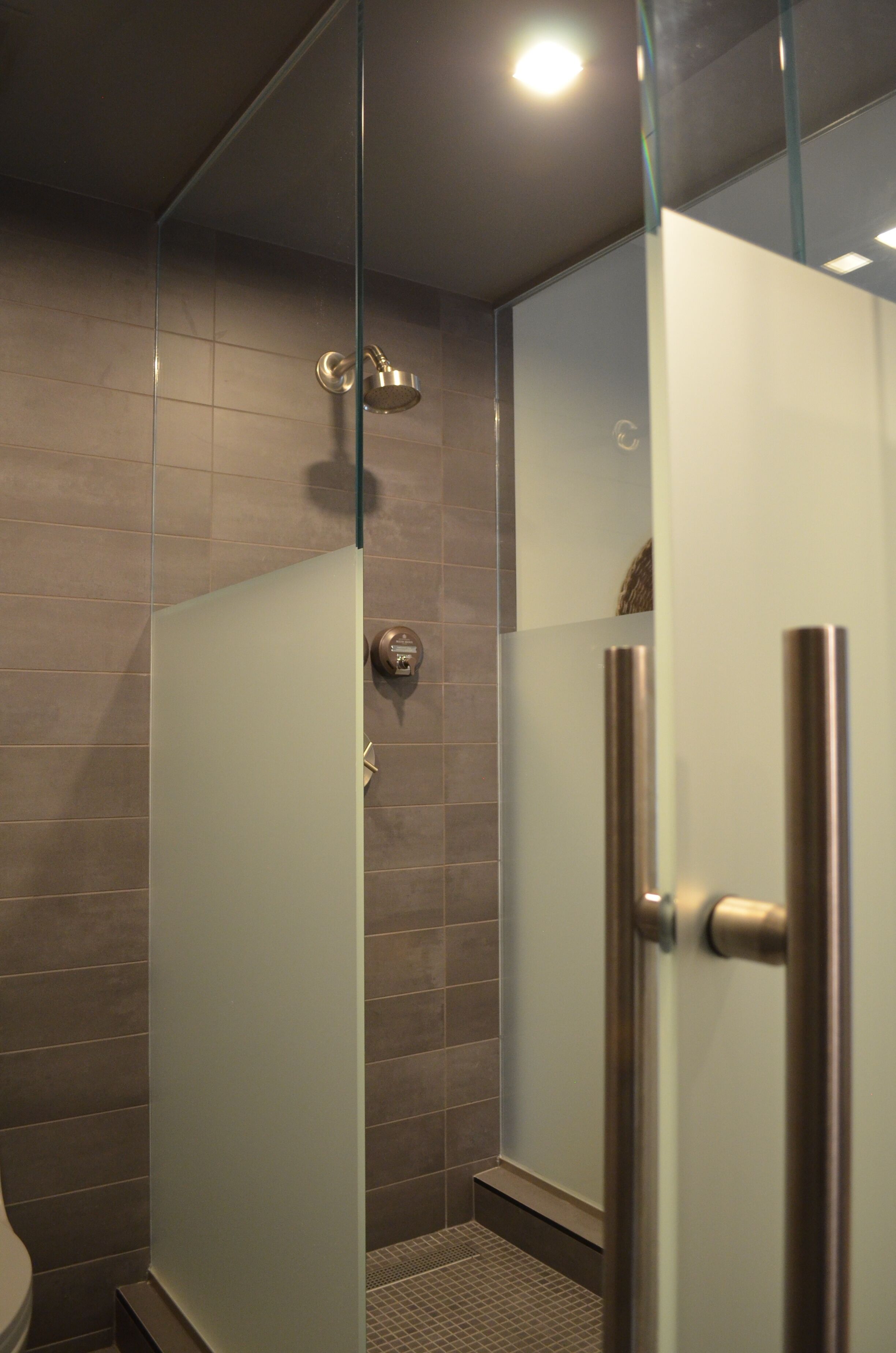 A modern bathroom with a glass-enclosed shower, tiled walls, and a visible toilet.