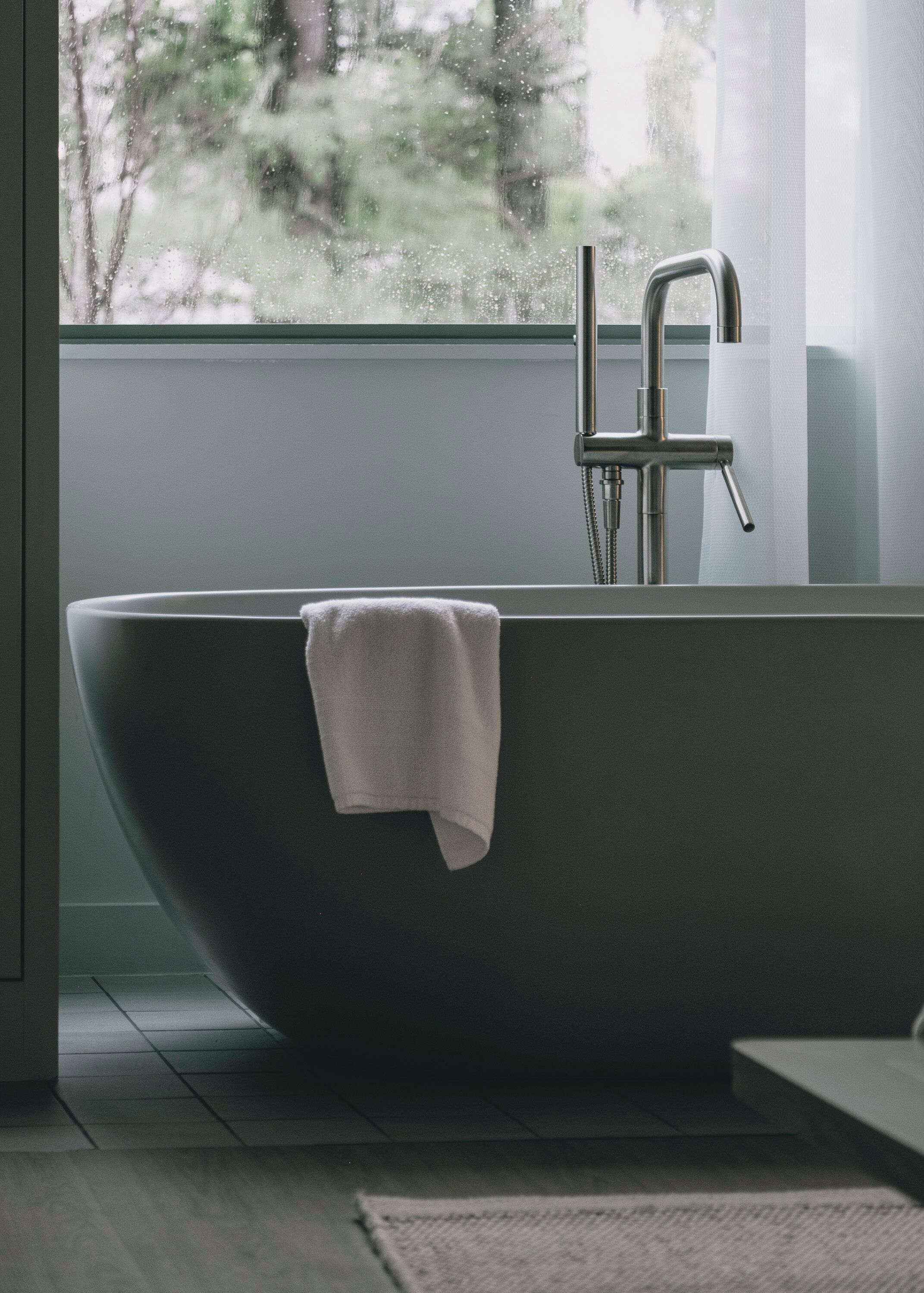 A modern bathroom with a freestanding bathtub, a visible towel, and a window with a view of trees.