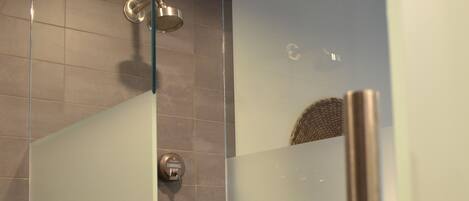 A glass-enclosed shower with a stainless steel showerhead and a control panel.
