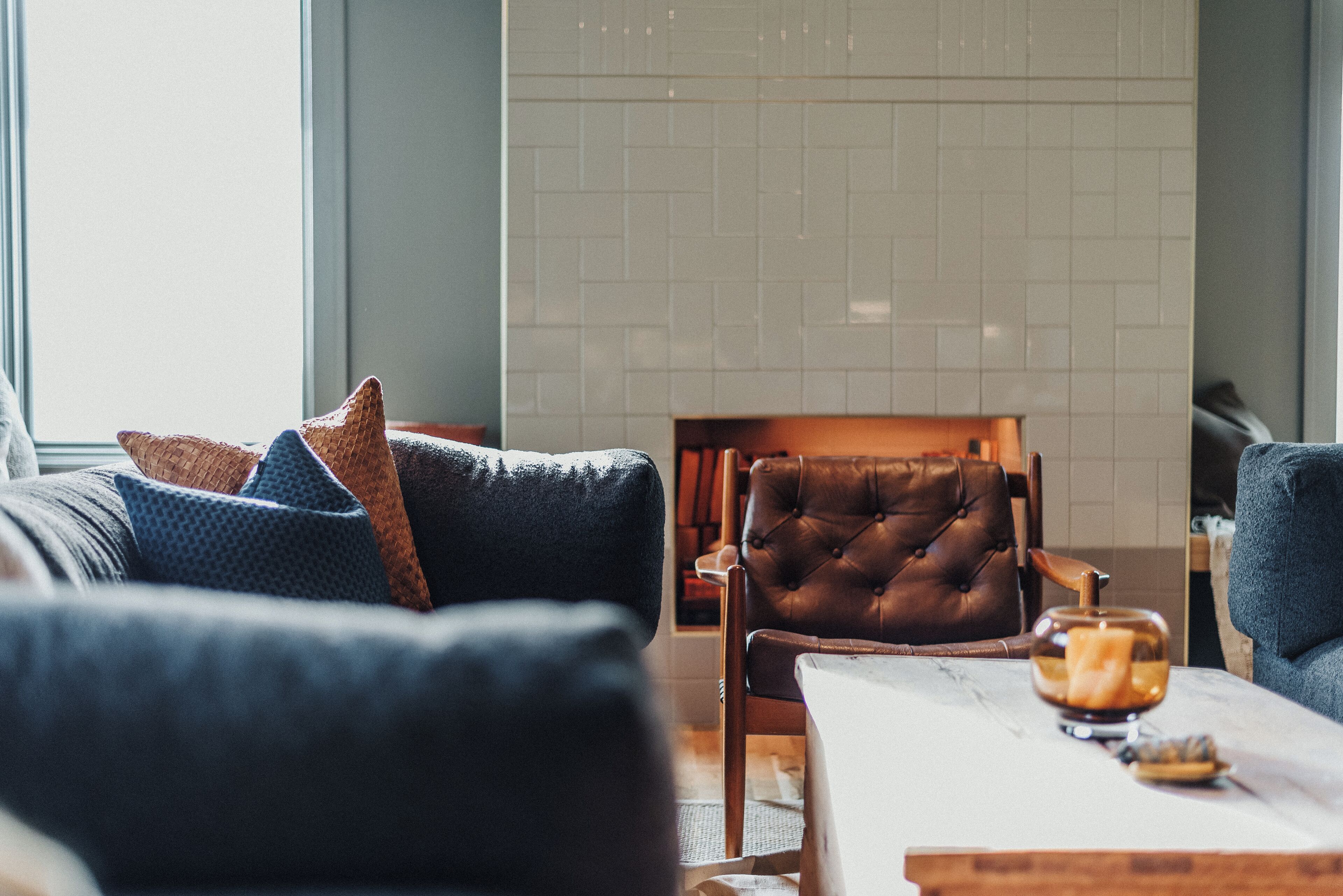 A modern living room with a dark blue sofa, a leather armchair, and a marble coffee table.