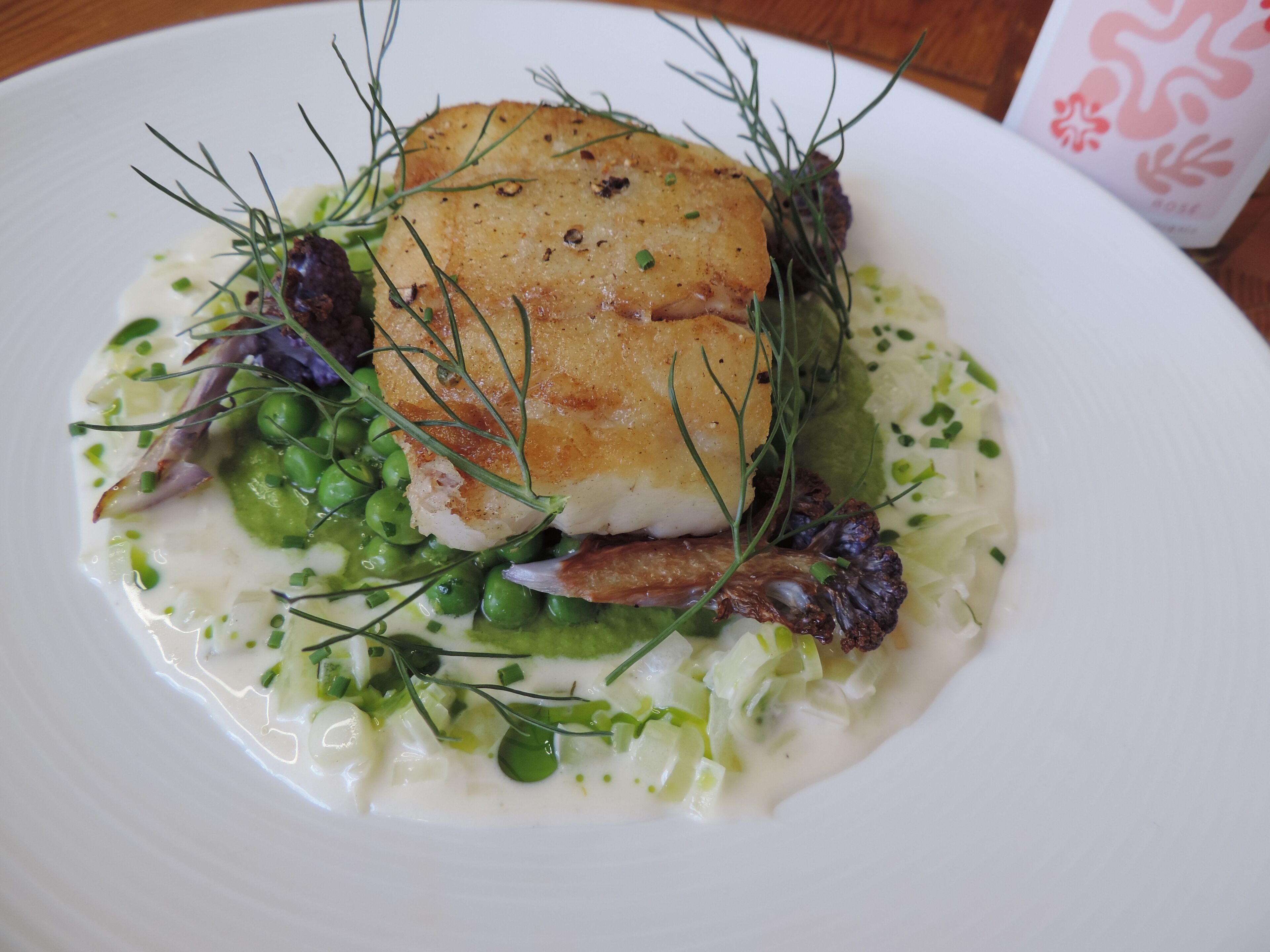 A plate of food with a piece of fish, peas, and greens.