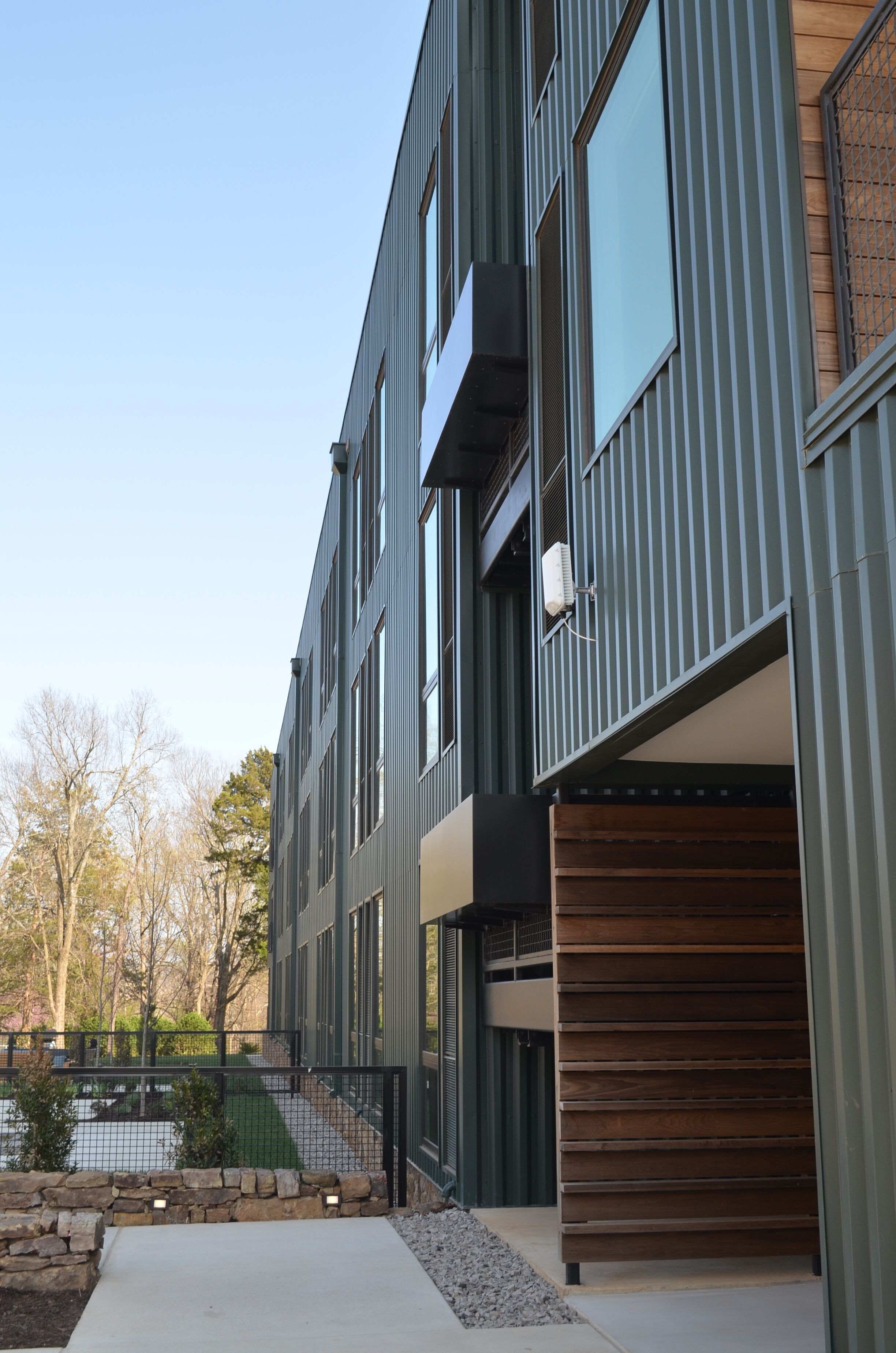 Un immeuble moderne à plusieurs étages, doté de grandes fenêtres, d’un garage et d’un chemin en pierre.