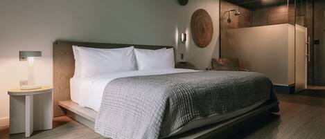 A modern bedroom with a large bed, bedside tables, a wall-mounted light, and a shower area.