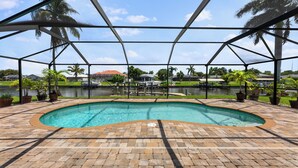 Una piscina amb una zona de maó al voltant, envoltada per una estructura de pergola metàl·lica.