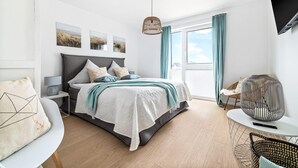 A modern bedroom with a bed, bedside tables, a hanging light, and a view of the outdoors. - Gorgeous apartment in Olpenitz (Olpenitz)