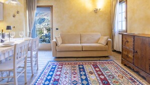 A living room with a beige sofa, a patterned rug, a wooden cabinet, and a dining area with a table and chairs.
