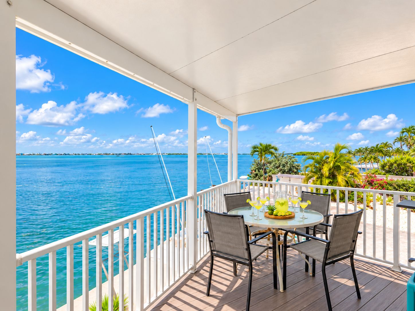 A covered outdoor seating area with a view of the ocean and palm trees.
