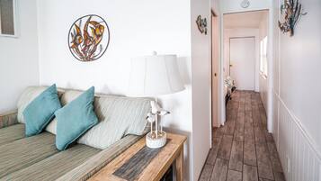 Ein Zimmer mit einer Couch, Kissen, einer Lampe, einem Wandbild und einem Flur mit einer Tür.