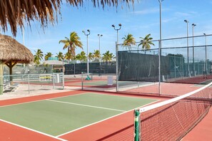 A tennis court with a net, a fence, and palm trees in the background.