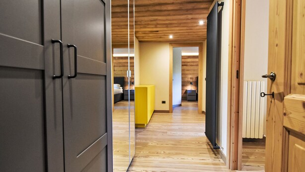 Un intérieur moderne avec un plancher en bois, un meuble jaune et un lit à l’arrière-plan.